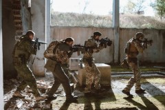 Side view of group of soldiers attacking abandoned building in danger war zone.